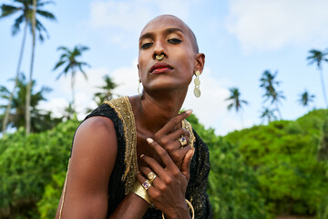 Trans sexual ethnic fashion model with brass jewelry accessories in elegant posture looks at...