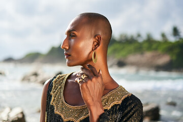 Outrageous black lgbtq person in luxury jewelry poses on scenic ocean beach. Non-binary ethnic...