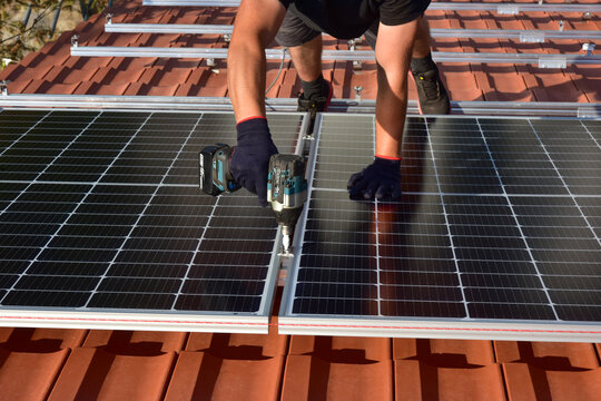 Dachdecker beim Aufbau einer Photovoltaikanlage auf einem neu gedeckten Ziegeldach: Verschraubung der Solarmodule auf dem Schienensystem