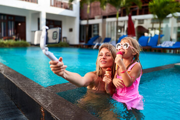 Blogger mom snaps selfie with daughter eating ice cream in pool at luxury resort. Smiling duo...