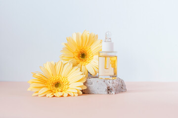 Cosmetic serum bottle on stone podium with yellow gerbera flowers on beige and white background....