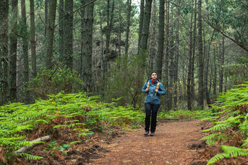 Young girl with backpack exploring a forest of pines and ferns looking curiously and admiringly at her surroundings, love of nature and sustainability, horizontal shot.
