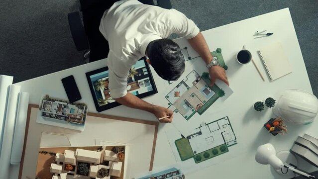 Top view of business man using tablet plan house design while sitting at meeting table with blueprint and equipment scatter around. Aerial view of civil engineer working at blueprint. Alimentation.