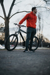 Fototapeta premium A young, active man standing with his bicycle in an urban park, embodying a healthy and relaxed lifestyle during his free time.