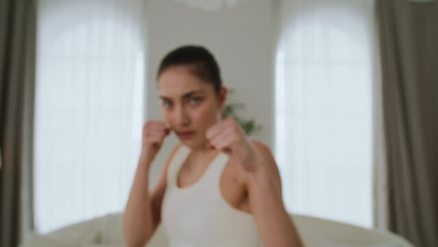 Slim and athletic girl in sportswear doing taekwondo exercises at home in living room. Young woman is practicing punches and kicks, doing martial arts. She is focused and determined