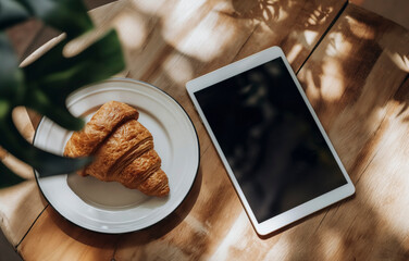 top view of a croissant is on a white plate next to a tablet - Powered by Adobe