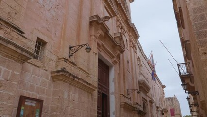 A walking shot showing a statue of the Virgin Mary holding Baby Jesus on the corner of Carmelite Priory in Mdina, Malta