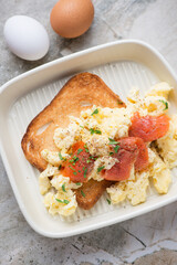 Scrambled eggs and smoked salmon on toast, vertical shot on a light-beige stone background, middle closeup, elevated view