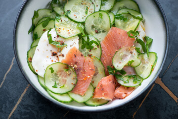 Bowl of cucumber salad with smoked salmon and poached egg, horizontal shot on a dark-green marble...