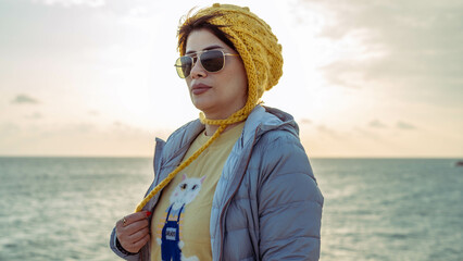 A woman with autumn style wearing a yellow hat and a blue jacket by the sea above the coral reef.