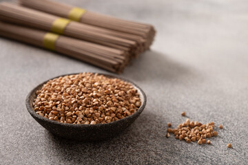 Uncooked buckwheat noodles soba and grain ion bowl on gray background. Space for text. Healthy vegan diet. Close up. Alternative gluten free pasta.
