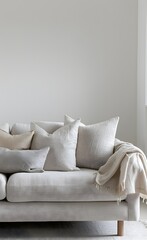 Fototapeta na wymiar A light gray sofa with soft cushions, beige blanket and pillows against a white wall