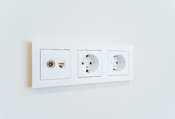 Three white electrical outlets mounted on a white wall