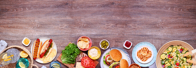 Summer BBQ or picnic bottom border with hamburgers, hotdogs, salad and snacks. Top down view over a...