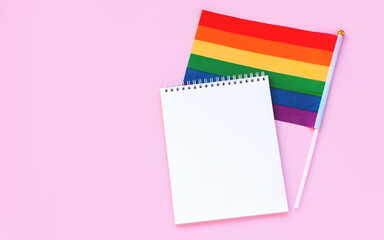 Blank mock up notebook on rainbow LGBTQ flag, pink background. June proud pride month parade, gay marriage, coming out day concept, human rights, tolerance. Flat lay, top view place for text or logo