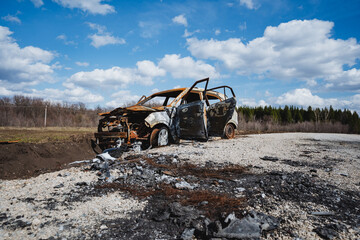 A burnt car is abandoned on the road in a field against the background of the sky, rusty iron,...