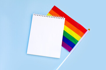 Blank mock up notebook on rainbow LGBTQ flag, blue background. June proud pride month parade, gay marriage, coming out day , human rights, tolerance concept. Flat lay, top view place for text or logo