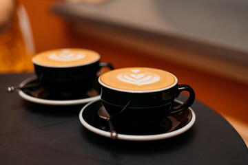 Two black cups of coffee on black table with latte art. Table in cafe outdoors. Concept of easy...