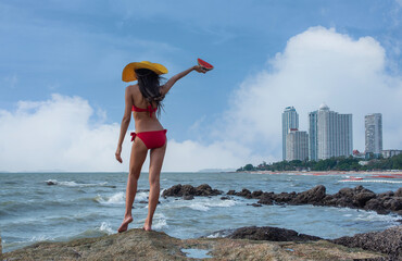 Young Asian female tourist wearing a sexy red bikini stands holding a piece of watermelon on a...