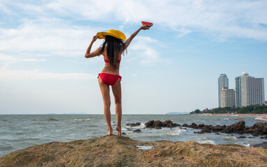 Young Asian tourist wearing a red bikini, wearing a brimmed hat, standing holding watermelon...