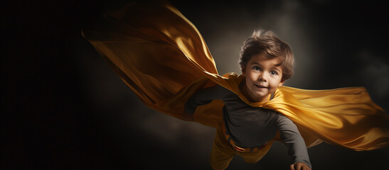 Un enfant aux cheveux blonds, souriant, habillé en Super-héros volant dans les airs, avec une cape jaune et un costume gris, image avec espace pour texte.