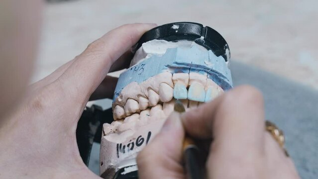 Dental technician coloring dental prosthesis with a paint brush at the laboratory, close-up view. Concept of implantats producing