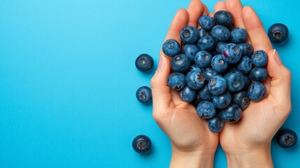   Person holds blueberries against blue backdrop, berries scatter image top - Powered by Adobe