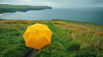   A yellow umbrella atop a lush green hill, beside a body of water, on a cloudy day