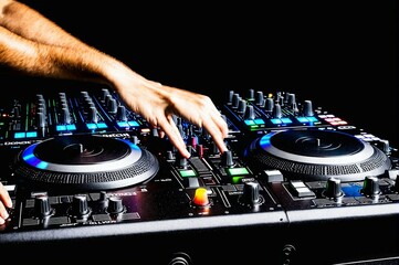 A DJ is playing music on a black mixer with a blue button