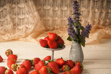 Strawberries and a vase with flowers on a wooden table. A wonderful summer picture of flowers and...