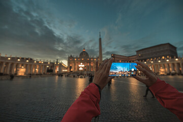 A person standing in front of a grand building at night, holding a camera up to capture its...