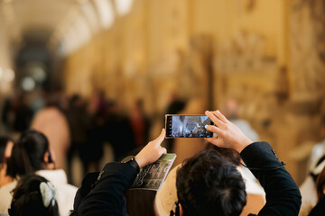 In a bustling crowd, a woman with a camera raised to her eye focuses on capturing the essence of the diverse group of people around her - Powered by Adobe