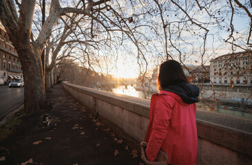 A woman stands gracefully on a bridge, gazing serenely at the water below. The tranquil scene...