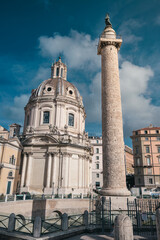 Fototapeta premium A tall, slender pillar stands proudly next to a towering modern building, creating a striking contrast of old and new architectural styles in an urban landscape