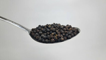 dry black pepper seeds on a spoon