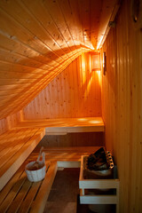 Gem&uuml;tliche Sauna mit Saunaofen und H&ouml;lzernerm Saunak&uuml;bel mit Holzkelle in warmen Licht.