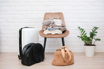 Travelling bags, suitcase, woman clothes on chair ready for trip in light livingroom.