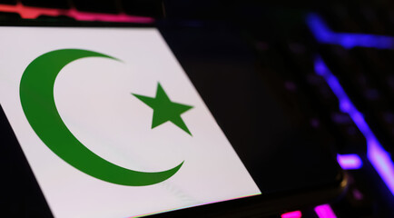 Crescent moon and star islam symbol on smartphone screen with computer keyboard (focus on center of...