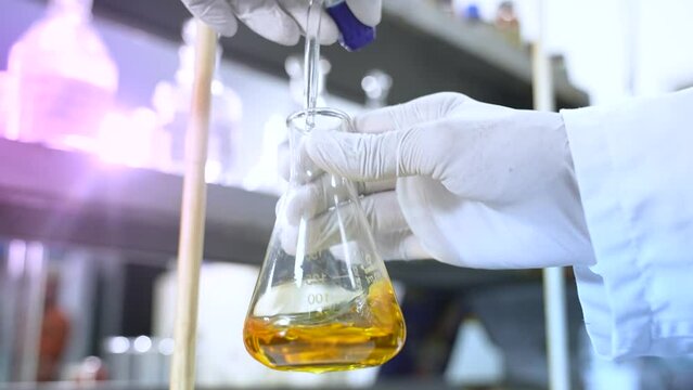 chemical mixing in a flask. scientist conducting science experiment in a beaker, flask. titration process with colorful yellow liquid in lab with other chemicals in containers. 