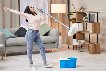 Happy, woman and cleaning floor by singing with mop by dance to relax at home for hygiene routine . Smile, housewife and microphone with music for joy or health for wellness from virus or bacteria