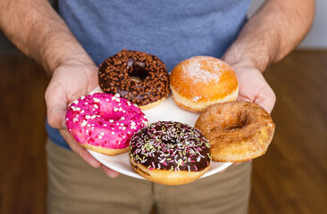 Various types of donuts on the plate closeup in male's hands. 