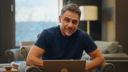 Casual mid adult man with laptop computer in home office, banking online, remote working. Portrait...