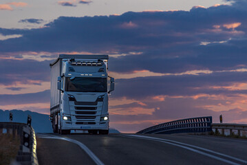 Truck seen from the front on a change of gradient and with a sunset sky in the background, vehicle...