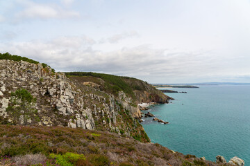 Les falaises abruptes se dressent majestueusement au-dessus de la mer d'Iroise, tandis que des nuages jouent avec les nuances de gris dans le ciel, créant une atmosphère mystique et captivante sur la 