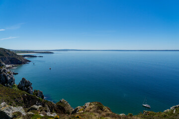 Des falaises escarpées de la presqu'île de Crozon, la mer d'Iroise se déploie en une étendue bleue infinie, ponctuée par quelques embarcations, sous un ciel radieux d'une belle journée d'été.