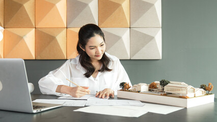 Portrait of beautiful young architect engineer measures house model while taking a note on...