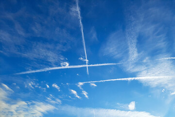 Bright blue sky with clouds and condensation trails left by passing airplanes. Contrail and white...