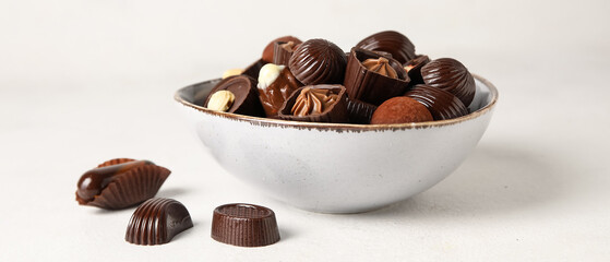 Bowl with chocolate candies on white background
