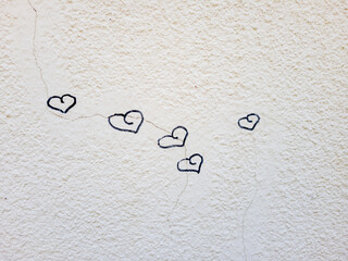 Cinq coeurs dessinés au feutre sur un mur blanc texturé