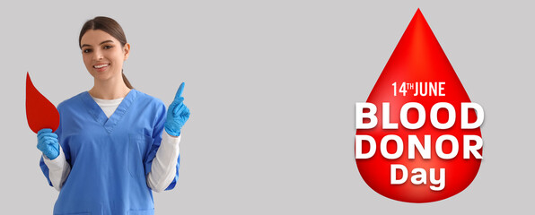 Female nurse with paper blood drop pointing at something on light background